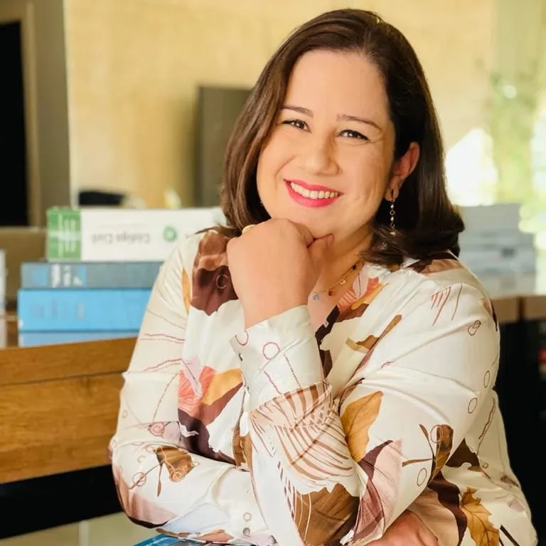 Retrato de Márcia Marques, advogada, sorrindo, com a mão apoiada no queixo, ao lado de livros de Direito